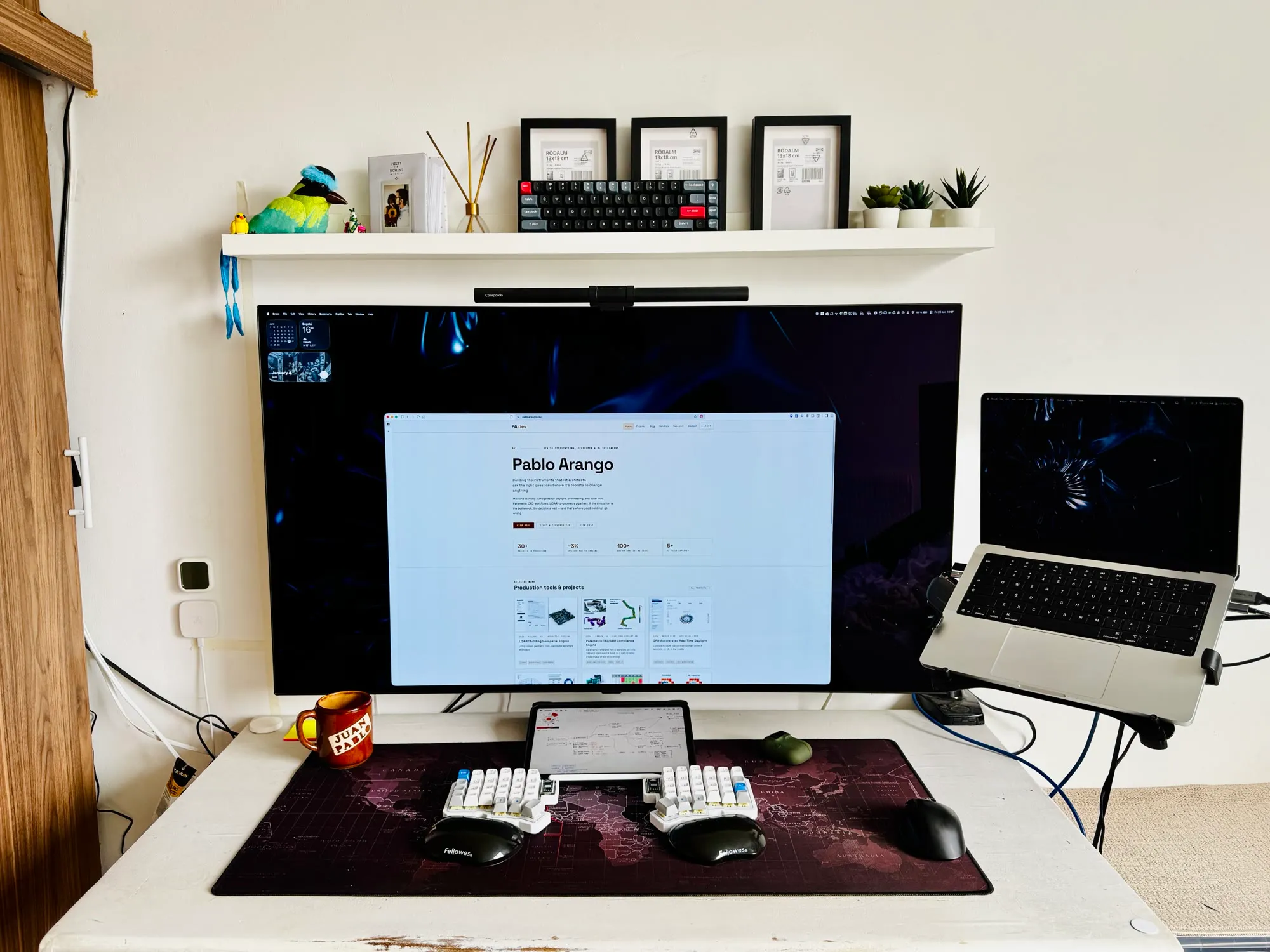 A split keyboard and tablet on a desk below a screen showing the portfolio site